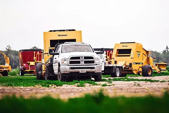 Vermeer balers being pulled by flaatbed pickups with net wrap on them.